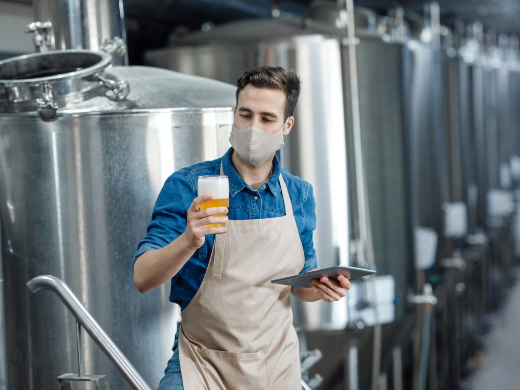 Brewer standing in a brewery production area with stainless steel fermentation tanks, illustrating beer filtration methods