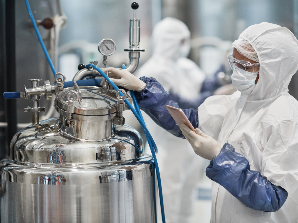 Technician in cleanroom gear checking a stainless steel pharmaceutical water vessel